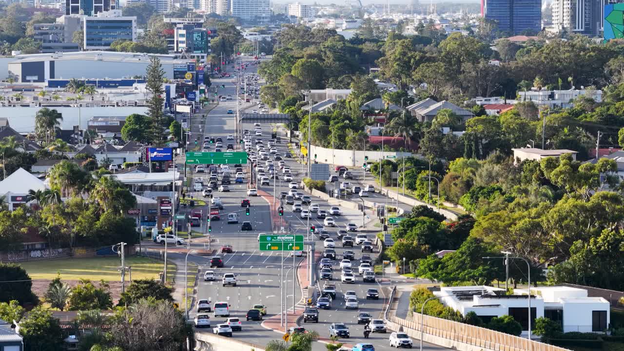 Drone footage captures bustling highway traffic amidst urban landscape and greenery in Gold Coast, Australia, under bright daylight