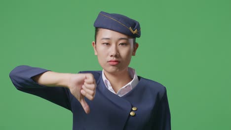 녹색 스크린 배경 스튜디오에 서있는 동안 카메라에 엄지손가락을 아래로 표시하는 아시아 여성 에어 호스테이스의 클로즈업