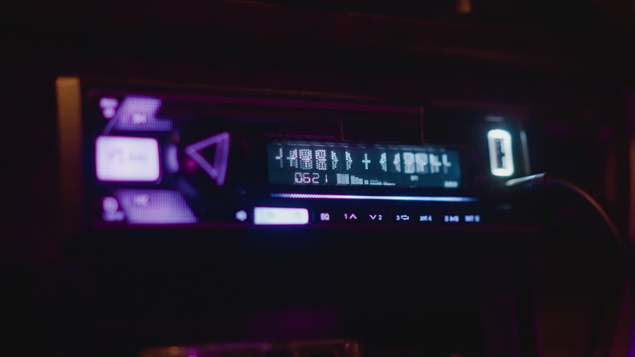 Autoradio neon che si illumina sul cruscotto, primo piano a mezzanotte del display digitale illuminato e dei pulsanti luminosi, retroilluminazione viola e ciano, cavo USB collegato alla porta, atmosfera ambientale di un viaggio a tarda notte
