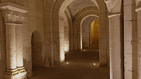 medieval stone crypt with arched corridors and columns, illuminated with warm lighting