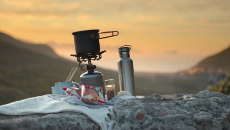 Bokeh-shot-of-camping-cooking-utensils-placed-on-a-mountain-ridge-with-a-blurry-background-at-sunset