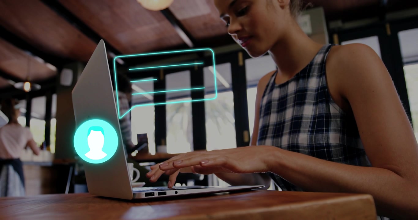 Donna che digita su un laptop in un caffè, avviando un avatar di chat color verde acqua che si anima sopra i tasti per una chat di lavoro.