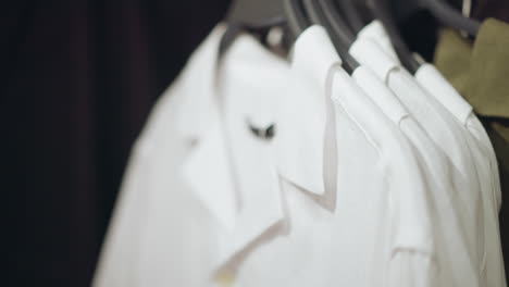 white lady s hand in a pink shirt returns a white shirt back to its position on the rack, where other white shirts are neatly arranged with a grey cloth next to them. background is slightly blurred