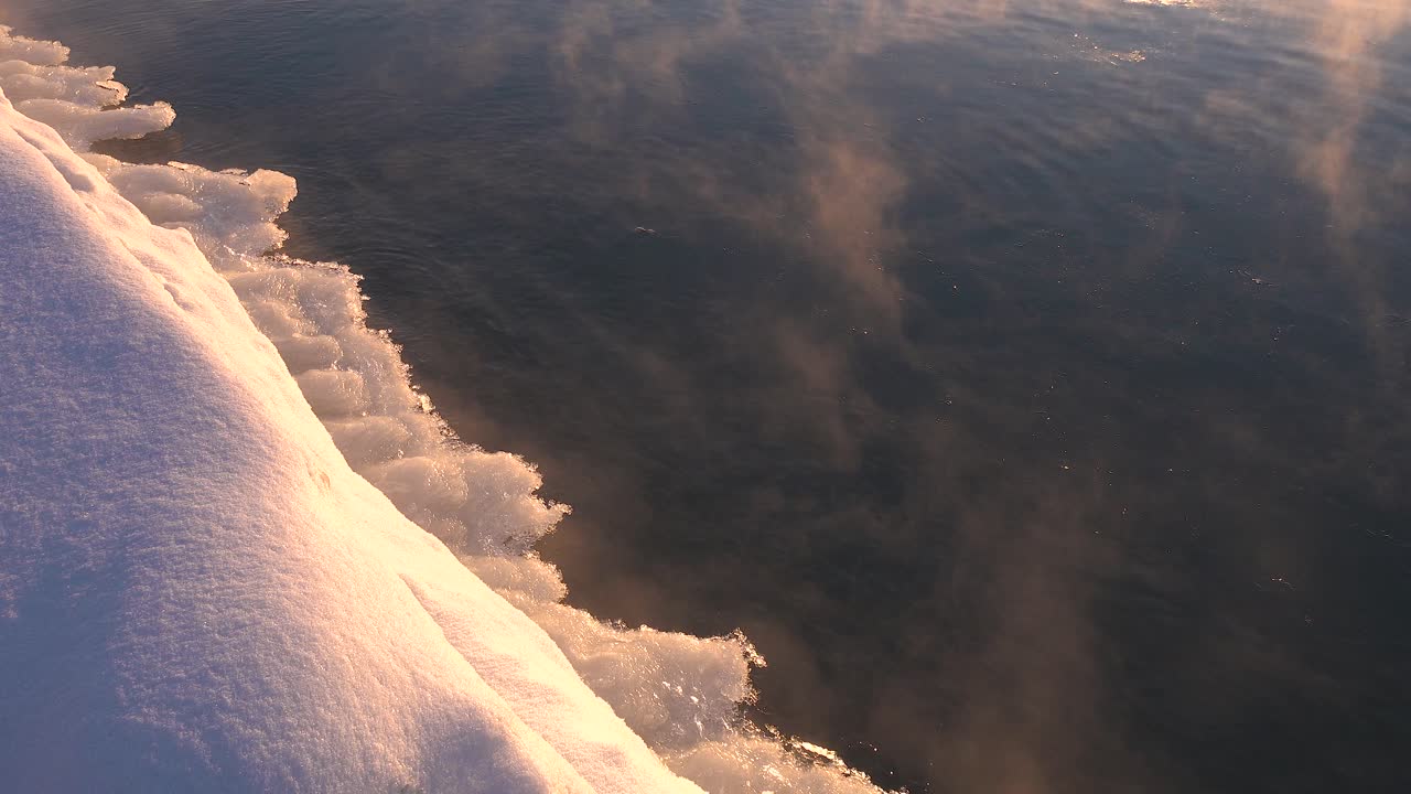 close up of ice forming on a frozen lake next to a snow covered shore in winter