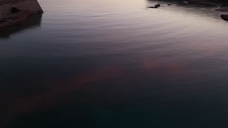 Last-light-on-horizon-casts-glow-across-gentle-calm-ocean-water-at-entrance-of-rocky-Mediterranean-bay