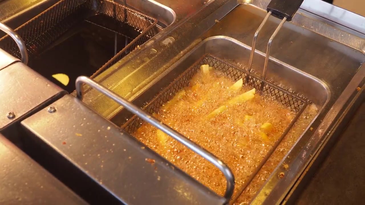 Pomfritter frituresteges i varm olie i en kommerciel frituregryde