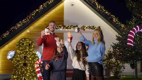 family celebrating christmas in front of decorated house at night