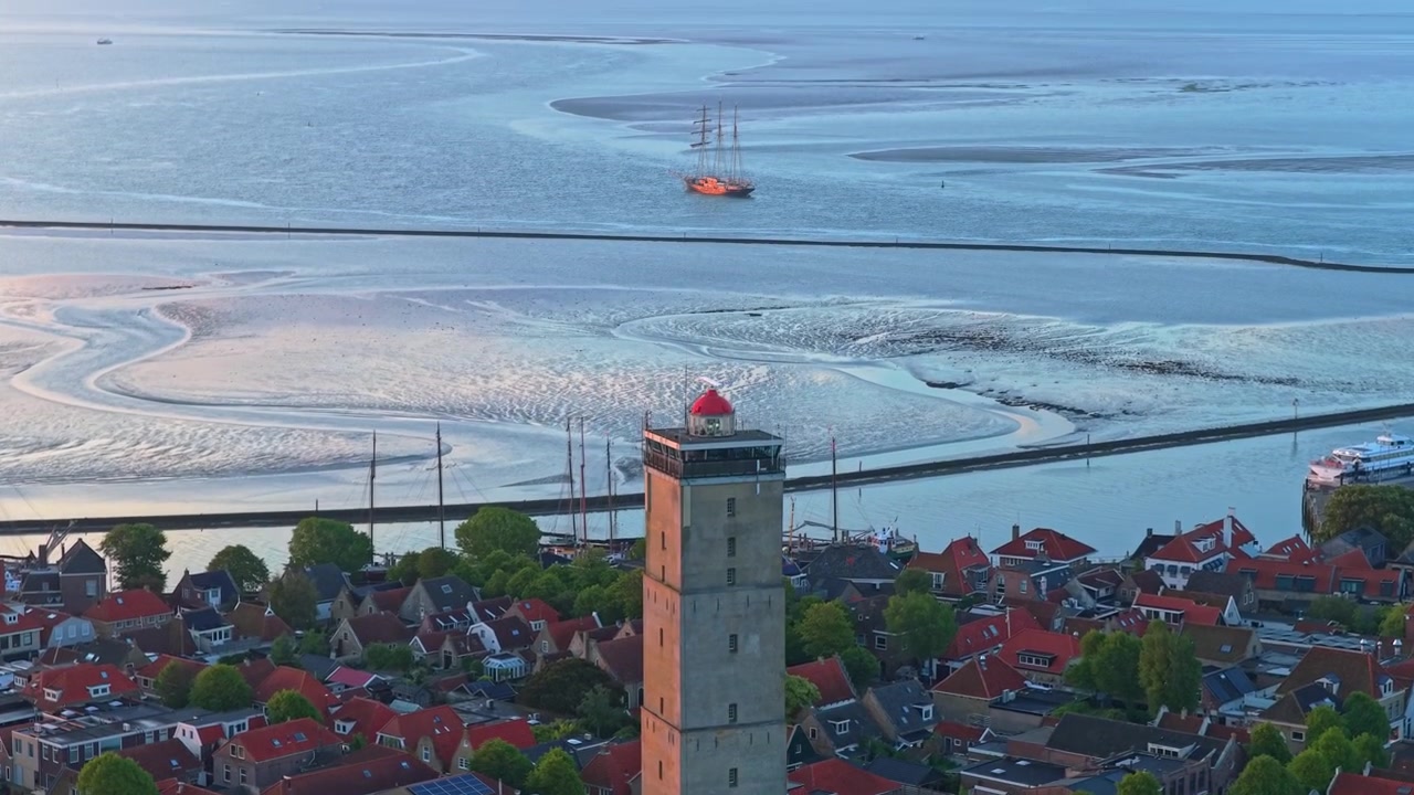 Sejlskib sejler nær Terschelling ved solopgang med Brandaris fyrtårn