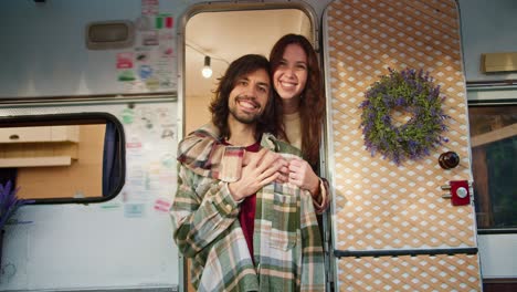 Portrait:-Happy-brunette-girl-hugs-her-brunette-boyfriend-with-stubble-in-a-Green-checkered-shirt-and-a-red-T-shirt-while-standing-near-her-trailer-during-her-picnic-outside-the-city-in-the-summer-at-the-camp