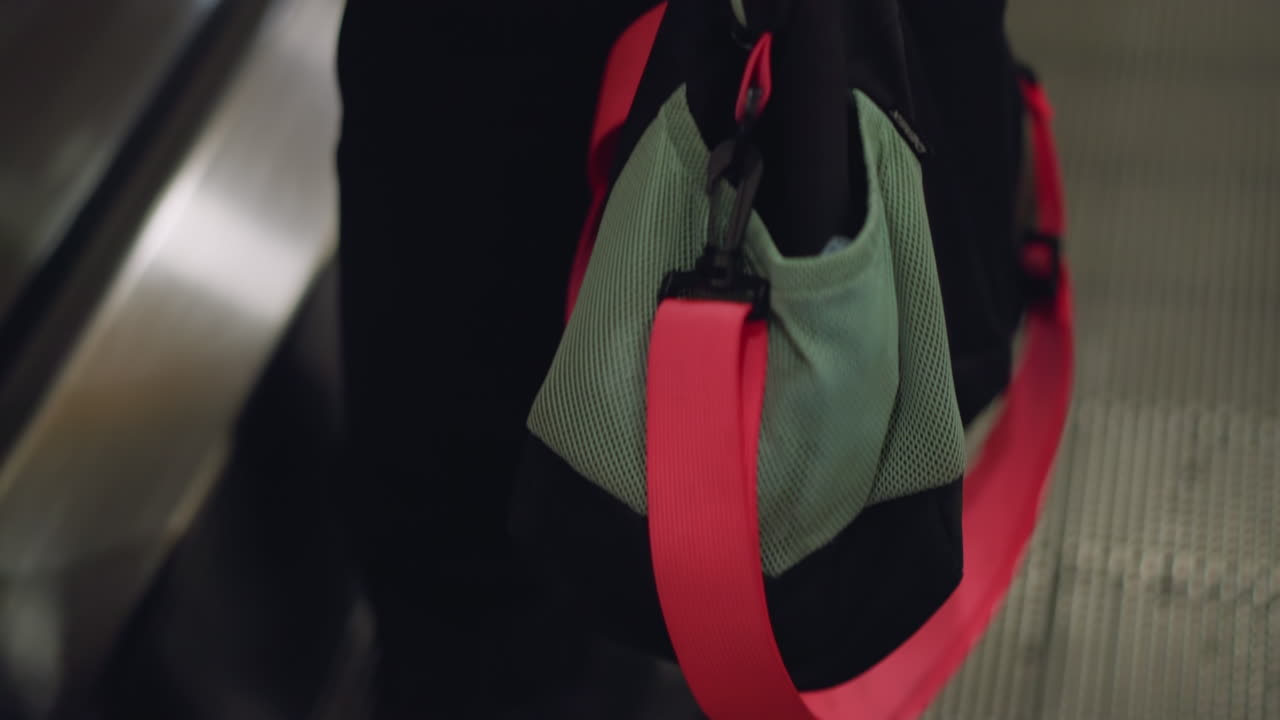 Close-up view of a backpack or gym bag with a prominent red strap, positioned on an escalator step. and the metal ridges of the escalator
