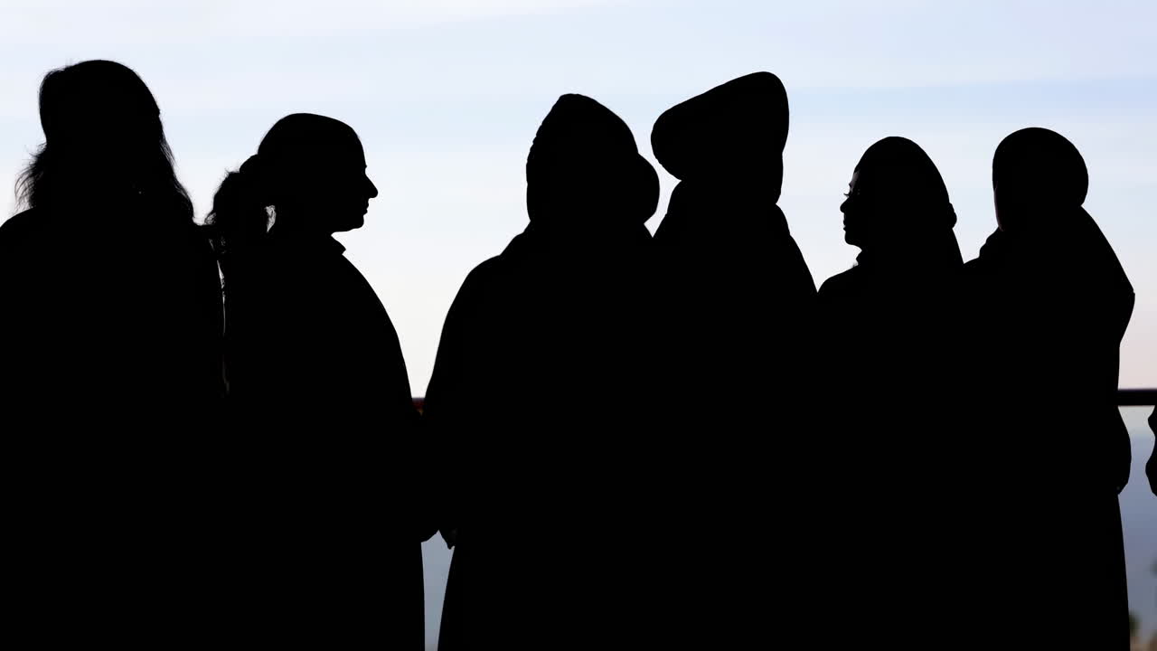 Dunkle Silhouetten von Menschen, die vor einem hellen Himmel stehen