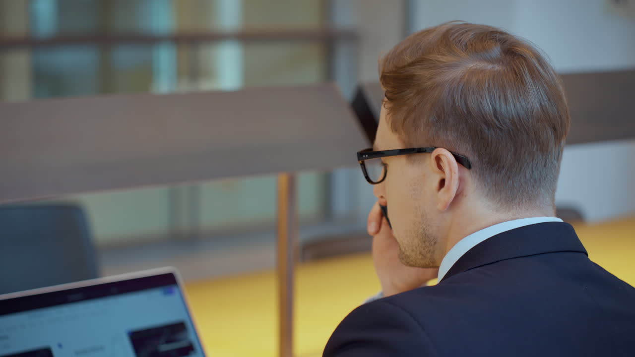 Empresário falando ao celular sentado no escritório - vista por cima do ombro.