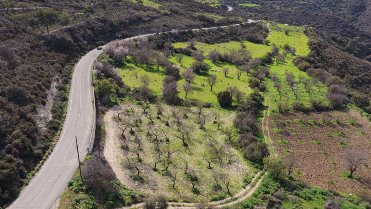 Aerial drone view of a car driving along winding road through green countryside in Lefkara, Cyprus