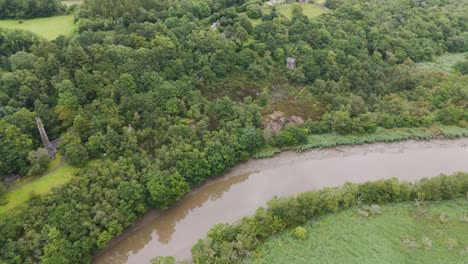 Drone-orbital-view-of-the-ruins-of-a-former-mine-situated-along-the-river-Tamar-in-Cornwall,-England,-highlighting-the-blend-of-history-and-nature