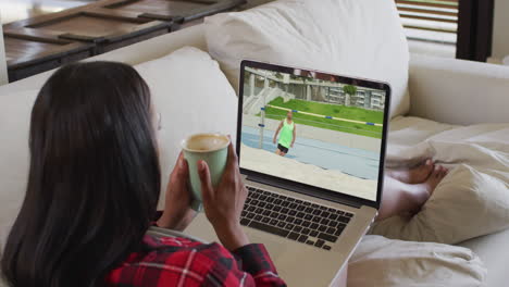 compuesto de una mujer sentada en casa sosteniendo un café viendo un evento de salto de altura en un portátil