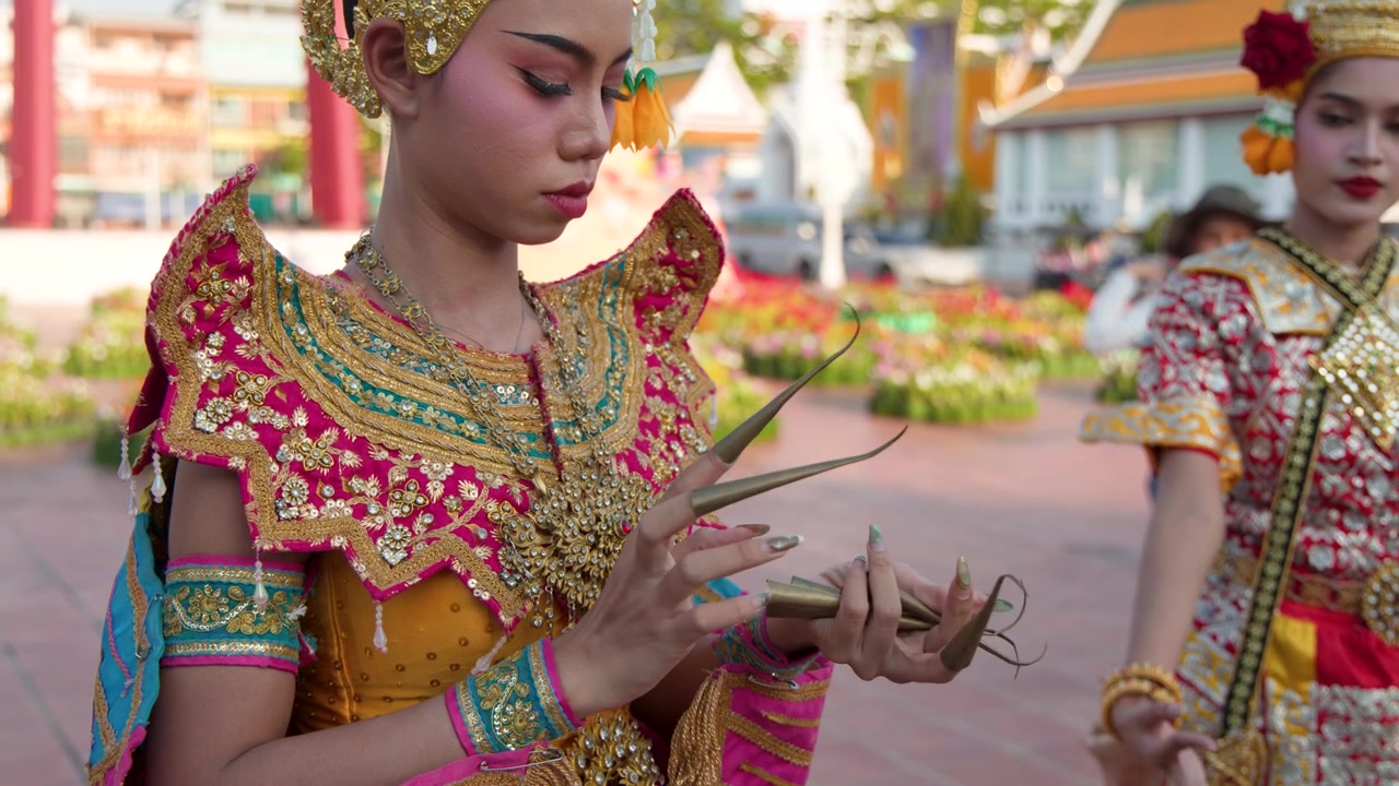 Una bailarina tailandesa con un elaborado traje tradicional se ajusta largas extensiones de uñas doradas al aire libre al atardecer