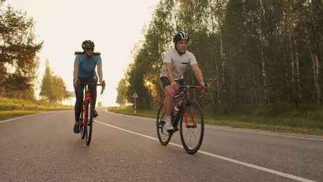 entrenamiento duro. triatleta dos ciclistas entrenando en bicicleta de carretera. dos ciclistas montados en bicicleta de ruta en el parque de la ciudad y preparándose para el triatlón. atleta fit entrenamiento intensivo dos hombres y mujeres en bicicleta antes de la competencia de triatlón