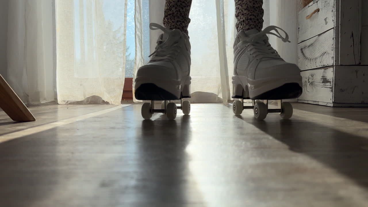Low angle view of a person rolling past the camera using shoes with retractable wheels on a wooden floor. Sunlight through curtains creates a dynamic indoor lifestyle and movement scene