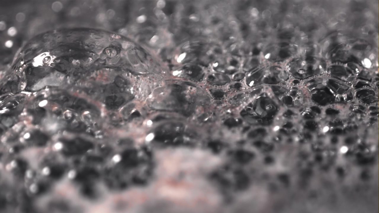 Primo piano macro di bolle che si formano e scoppiano su una superficie liquida