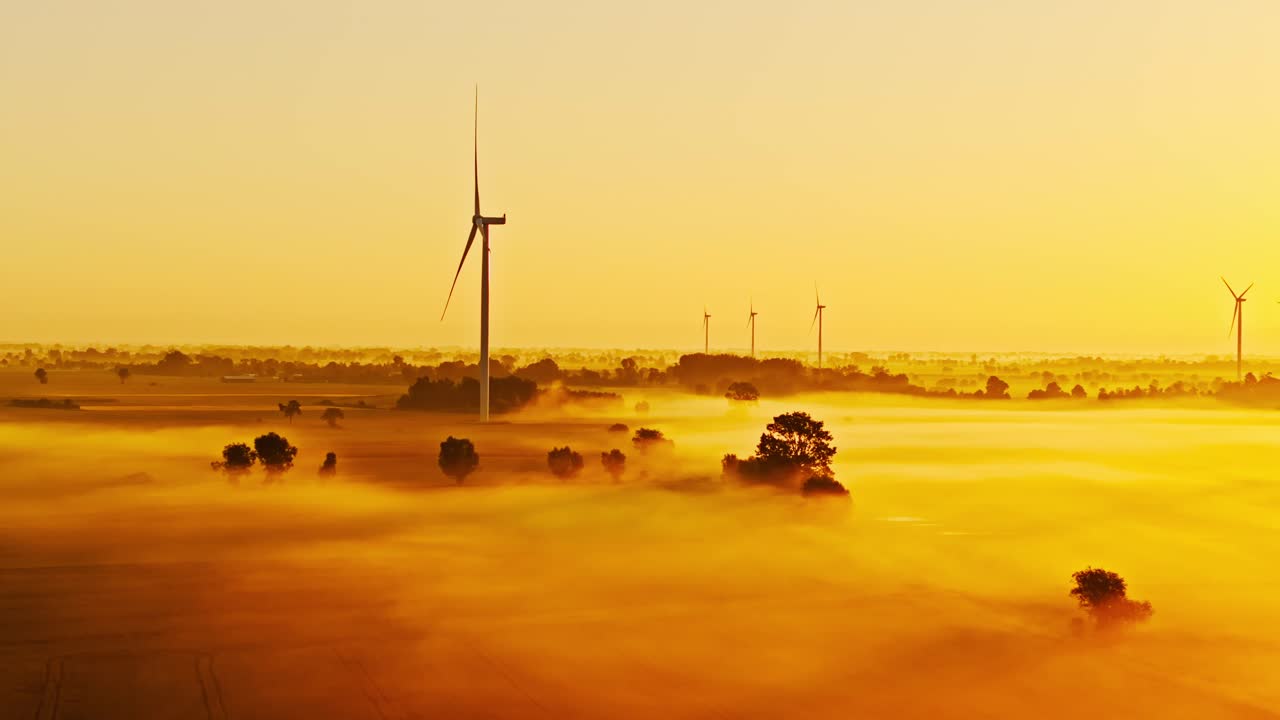 Soft mist and golden light merge as drone circles windmill in tranquil dawn