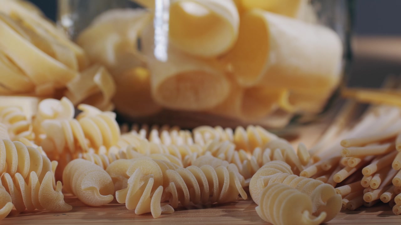 Varietà di pasta secca che cadono in un barattolo di vetro su un tavolo di legno