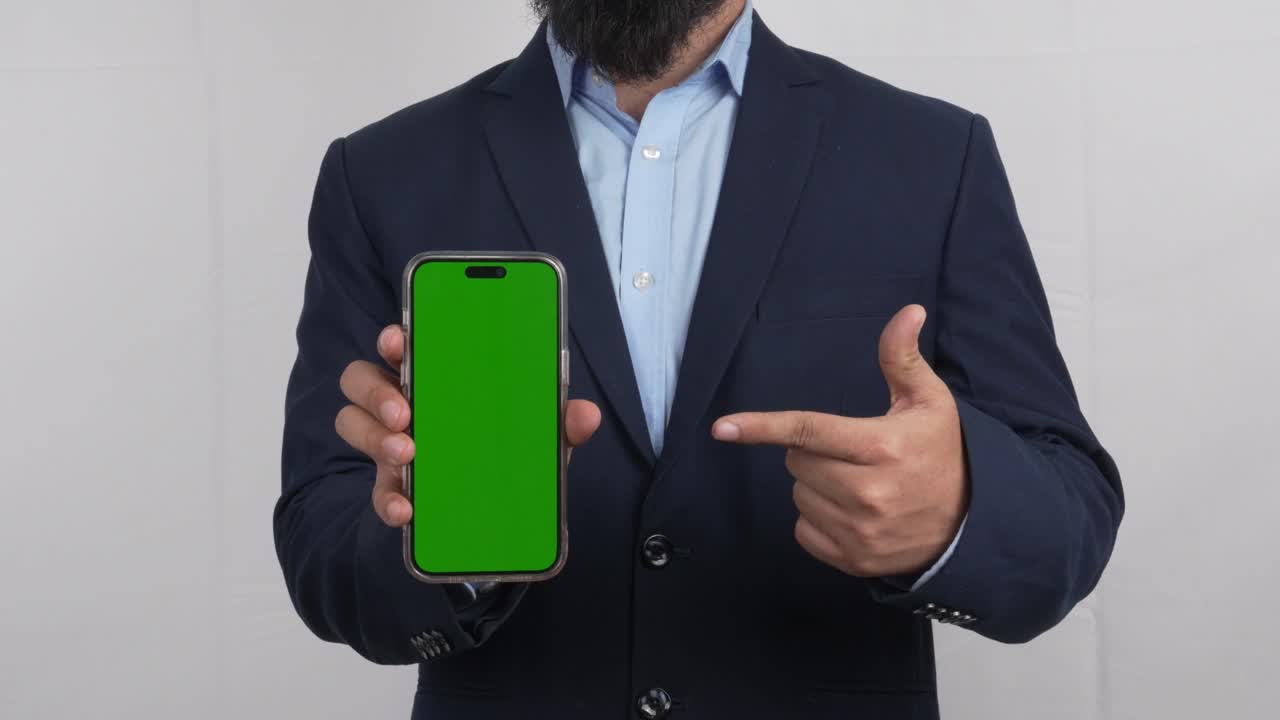 Uomo in abito che indica uno smartphone in modalità verticale con mockup di smartphone su schermo verde, Video 4K