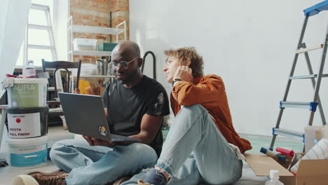 diverse couple looking for home renovation ideas on the internet in new flat