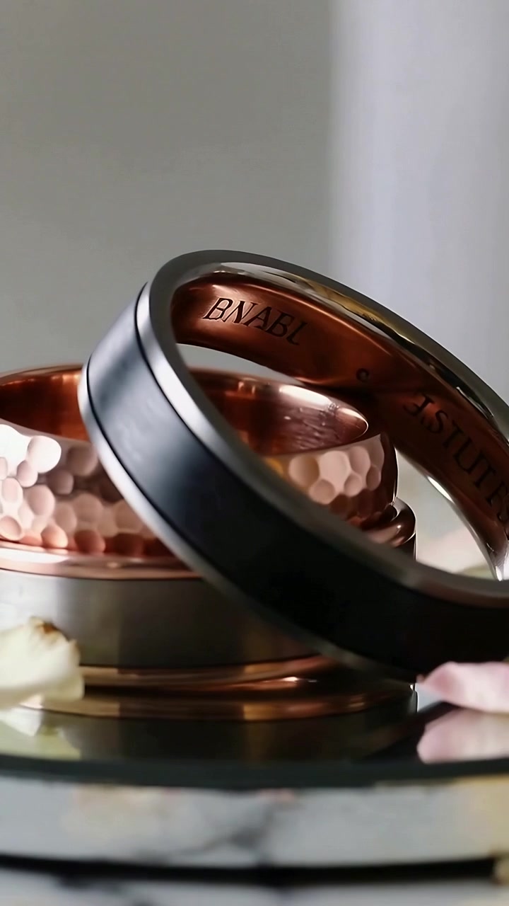 Vertical video: Tilting stacked trio of rings nudging on tray, showing black ring inner engraving