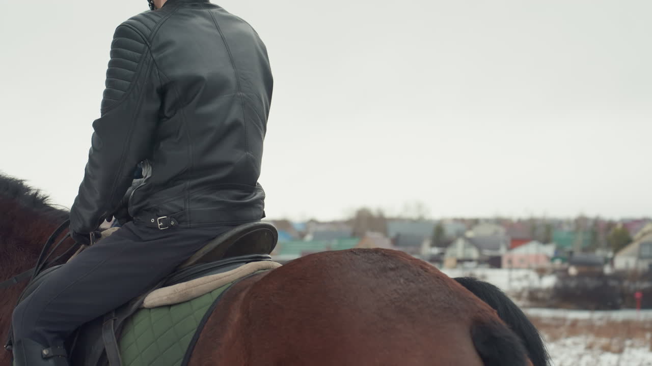 Addestramento a cavallo in tandem con istruttore che guida lo studente in una lezione di equitazione con casco attraverso un campo rurale innevato, istruttore con giacca di pelle accanto al giovane allievo, primi piani di profilo di sella e redini.