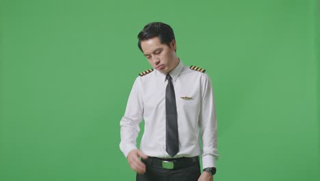 녹색 스크린 배경 스튜디오에 서 있는 동안 두통을 가진 아시아 남자 조종사