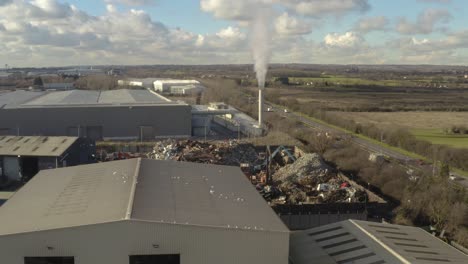 scrap metal factory with smoking chimney, birds on roof and cranes picking up metal