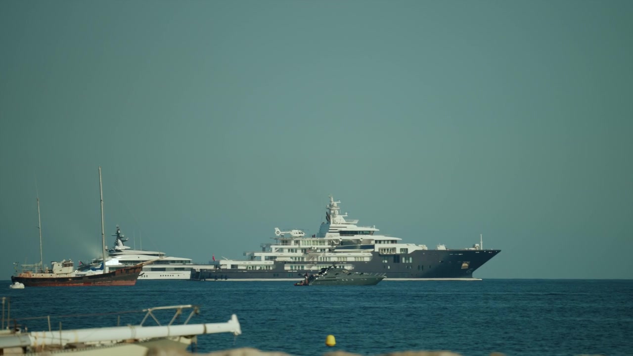 Grande superyacht in navigazione in acque aperte con imbarcazioni più piccole, a simboleggiare viaggi di lusso, ricchezza e trasporto marittimo.