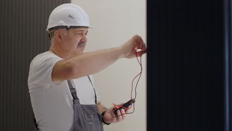 un hombre electricista comprueba el voltaje en la red con un probador de cables preparándose para instalar un hogar inteligente. retrato de un electricista en el interior moderno del apartamento