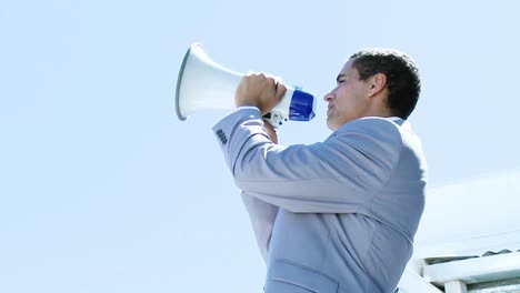 Young-businessman-shouting-into-a-megaphone-outdoors