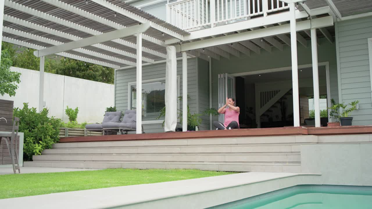 Breathing woman pink top on deck stretching lifting arms up joining palms lowering hands to chest