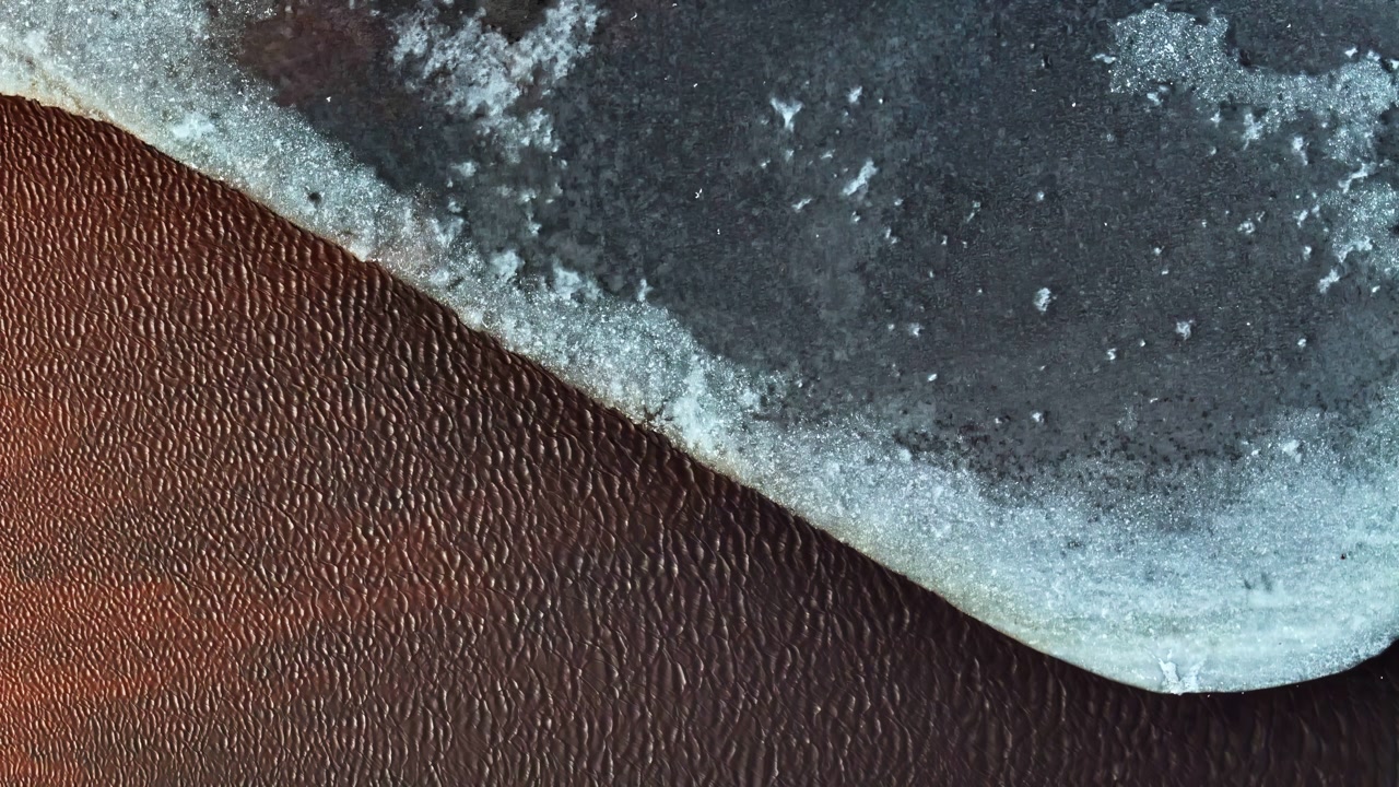 Abstract aerial shot of flowing water under frozen ice with rich textures and cold tones