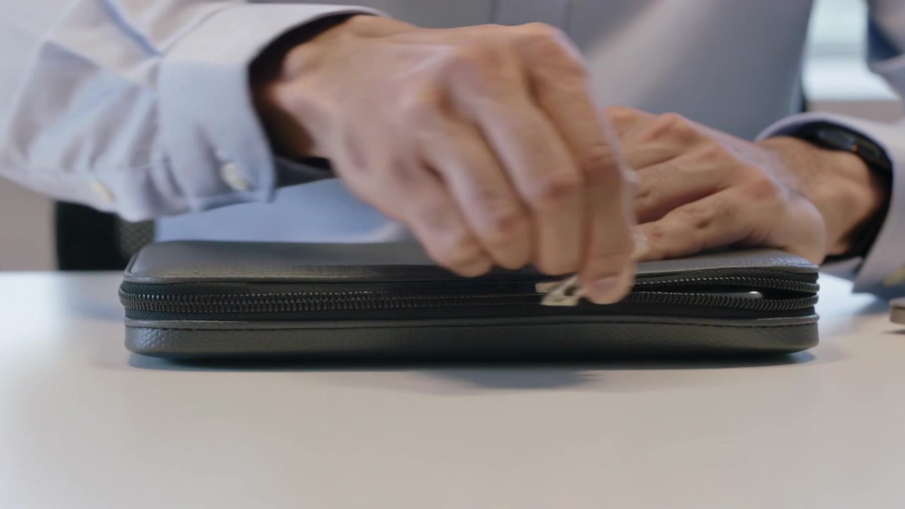 Reaching left hand wearing watch, shirt drawing zipper tab across sleeve at desk accessing laptop