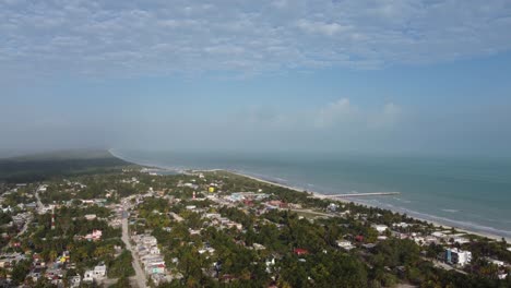 El-Cuyo,-Un-Pintoresco-Pueblo-Costero-En-La-Península-De-Yucatán-Con-Exuberante-Vegetación-Y-Un-Largo-Muelle-Que-Se-Adentra-En-El-Mar,-Durante-El-Día,-Vista-Aérea