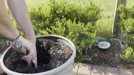 side view of a person digging a hole in a pot near bushes