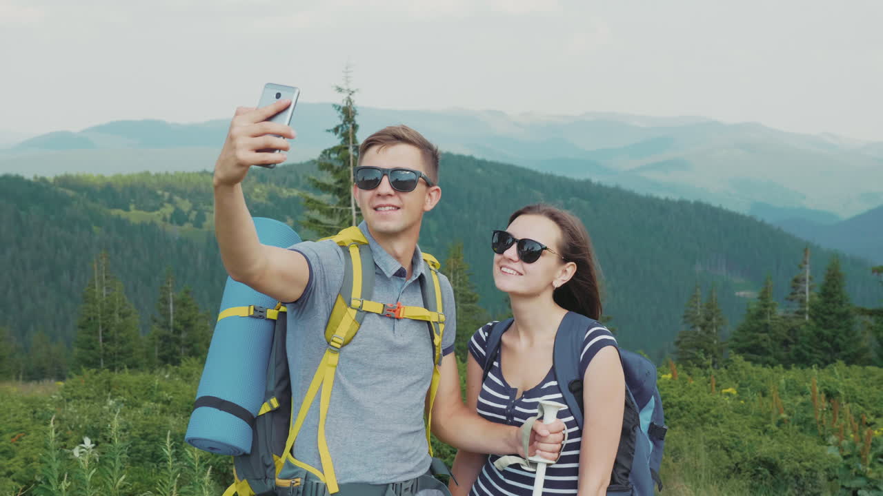 una pareja joven de turistas con mochilas se toman fotos con un teléfono inteligente en una hermosa