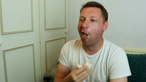 um homem comendo um sanduíche assistindo tv