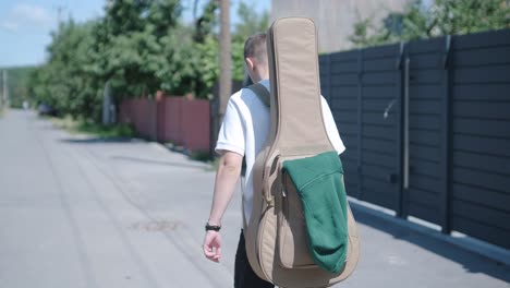 young man walking with guitar on street near forest