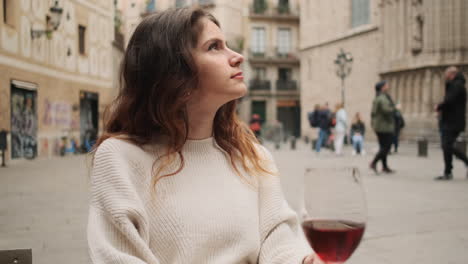 joven mirando a su alrededor mientras está sentada en un café con un vaso de vino rojo