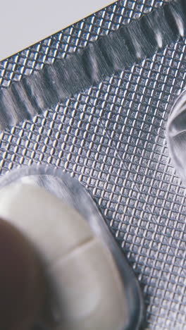 sick man taps with long silver blister of white oval medical pills on light surface extreme close view