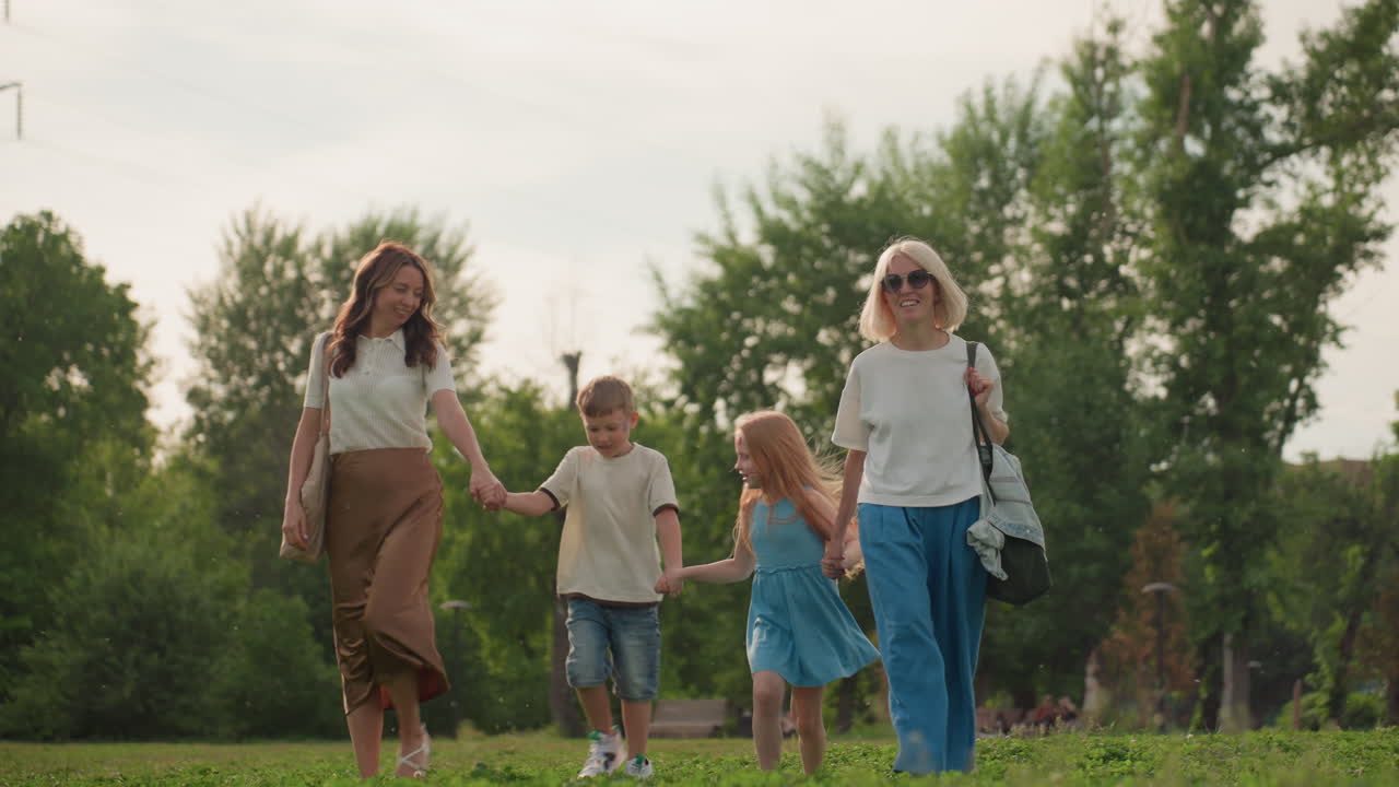 mothers with toddlers holding hands jumping happily in park, smiling children and parents enjoying outdoor family time on green grass, summer field play, joyful movement and bonding in nature