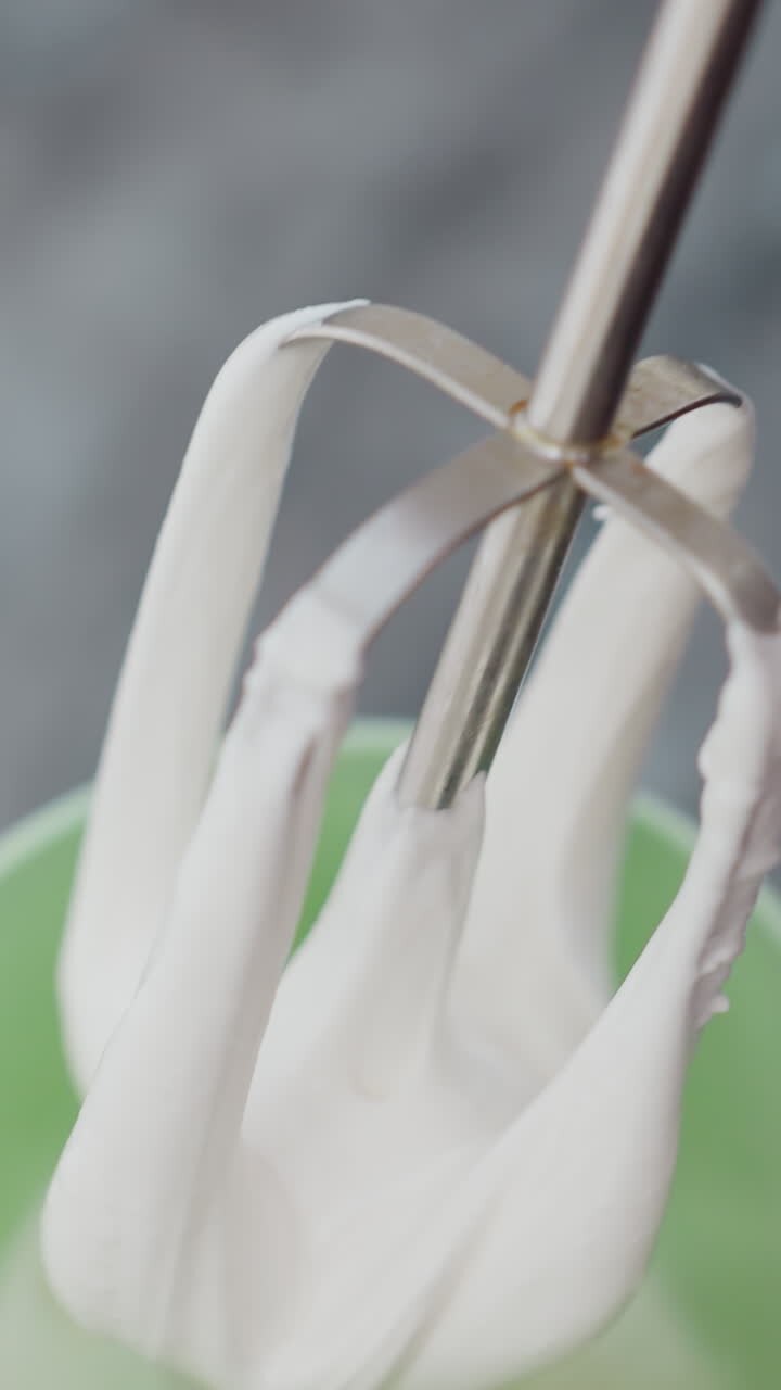 Close up of electric hand mixer in green cup, thick milk being brought out on mixer, preparing beverage, blending ingredients in kitchen setting, making creamy drink