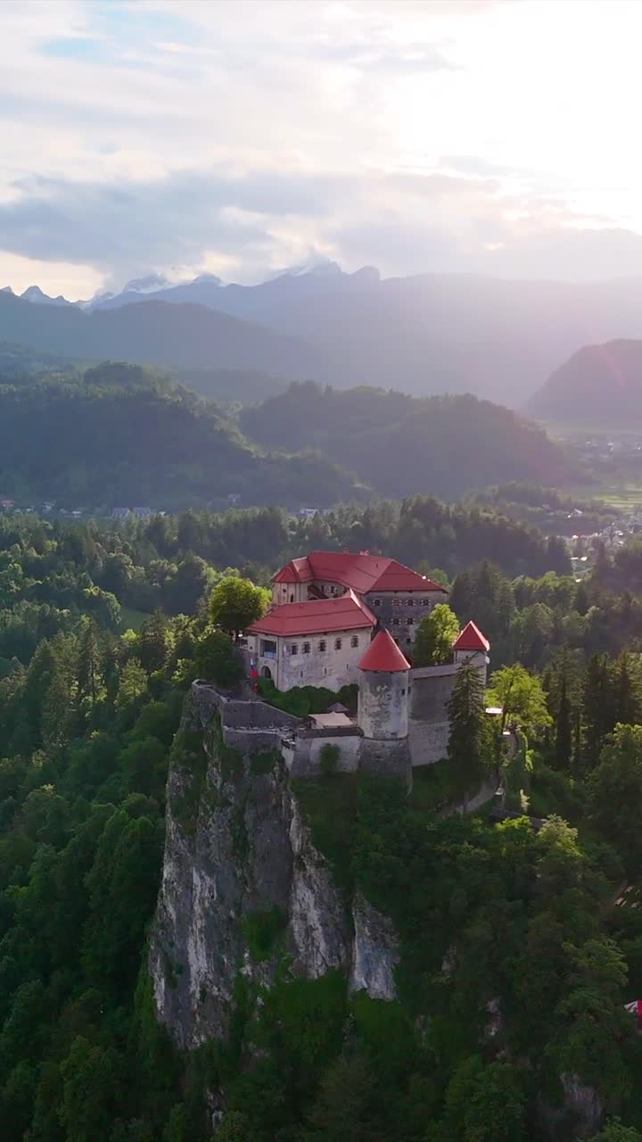 Ripresa circolare con drone del Castello di Bled con bagliori solari cinematografici, scatto epico verticale.