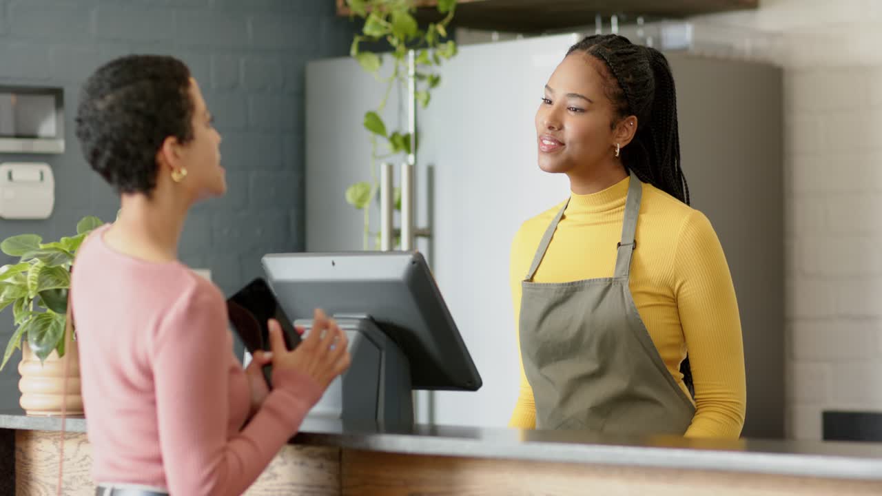 Female barista greeting customer at cafe counter after placing phone at QR code guiding payment