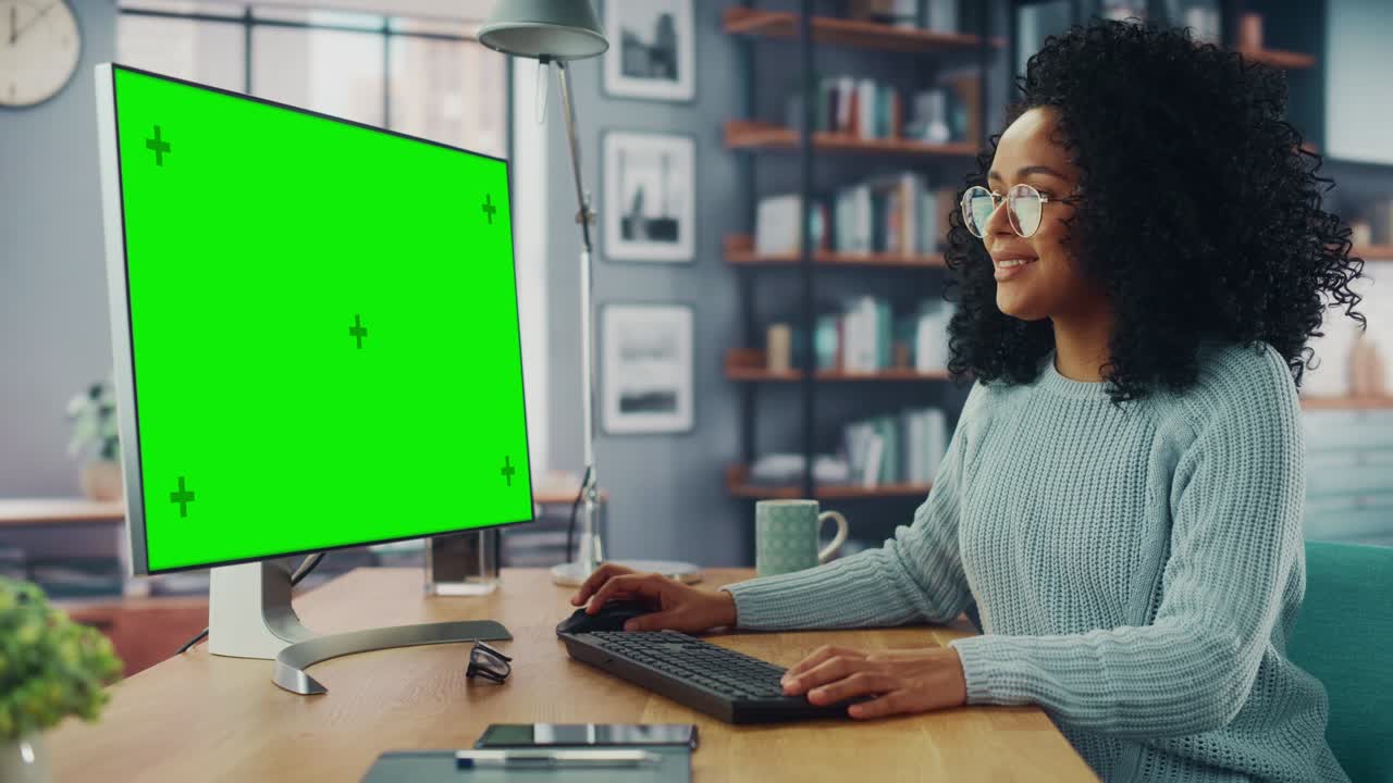 latina donna specialista che lavora su un computer desktop con schermo verde mock up display a casa salotto mentre è seduto a un tavolo. freelancer donna chiacchierare su internet sui social network.