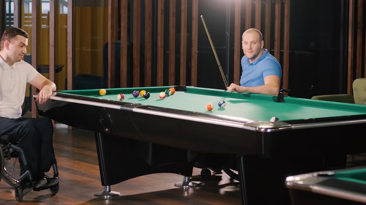 Adult men with disabilities in a wheelchair play billiards in the club